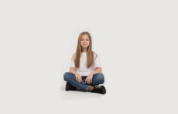 Ein schönes Teenager-Mädchen in einem weißen T-Shirt und Blue Jeans sitzt auf einem weißen Hintergrund