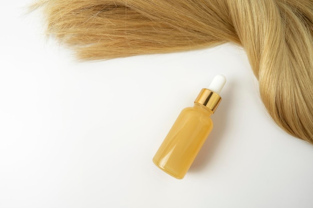 Ein Schönheitsserum mit Vitamin C oder Glättungsöl zur Pflege der Haare in der Nähe der blonden Haarsträhne