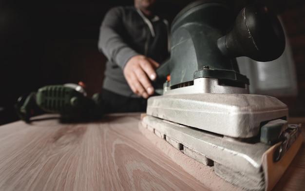 Ein Schreiner arbeitet in einer Werkstatt Schreinerschleifer Möbelherstellung Ein Schreiner schleift ein Holzteil mit einer elektrischen Schleifmaschine