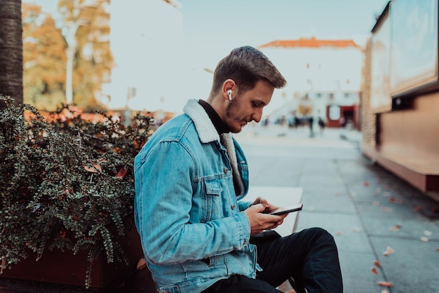 Ein schüchterner Student, der mit einem Smartphone und kabellosen Kopfhörern in einem Park sitzt