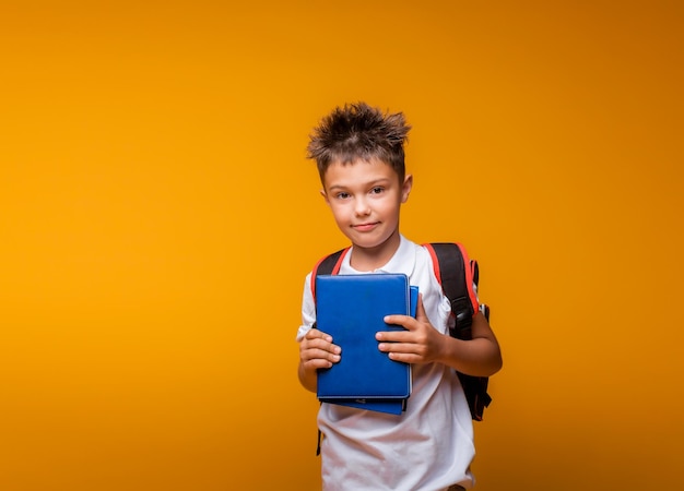 Ein Schuljunge hält ein blaues Buch auf gelbem Hintergrund zurück zur Schule