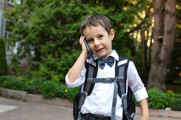 ein Schuljunge in einem weißen Hemd mit Rucksack telefoniert