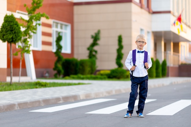 Ein Schuljunge mit blonder Brille und Rucksack steht in der Schule