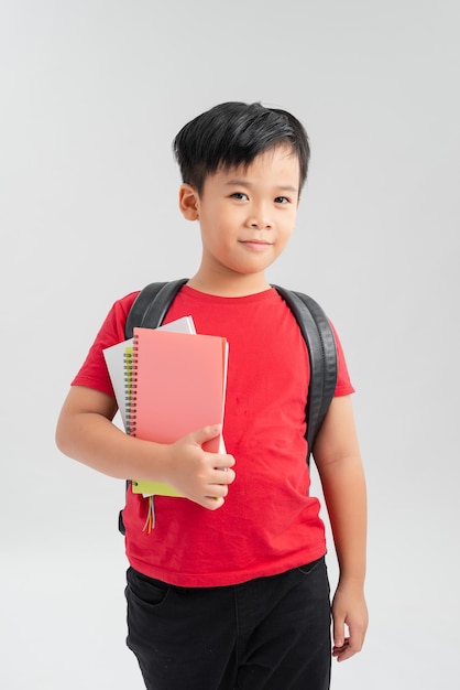 Ein Schuljunge mit Rucksack, der ein Notizbuch lokalisiert auf weißem Hintergrund hält