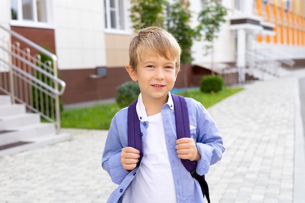 Ein Schuljunge steht mit einem Rucksack in der Nähe der Schule, lächelt, lacht Grundschule