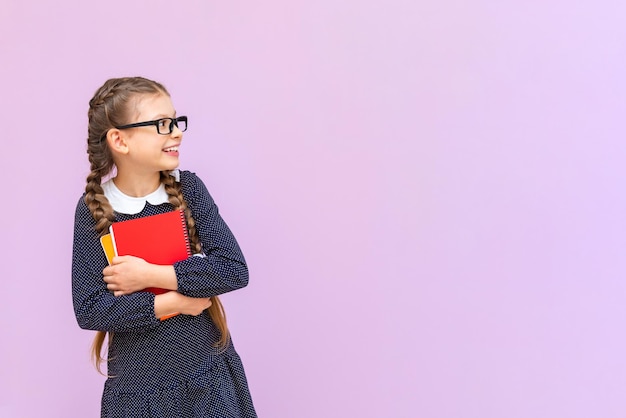 Ein Schulmädchen hält Notizbücher und zeigt auf Ihre Werbung auf einem rosa isolierten Hintergrund Bildungskurse für Sekundarschulkinder Kopieren Sie Platz