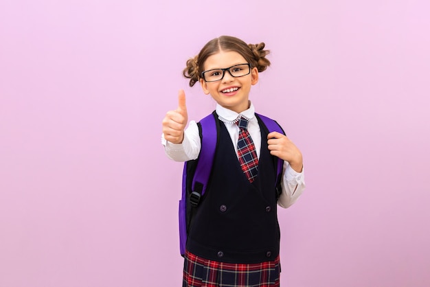 Ein Schulmädchen mit Brille auf einem isolierten Hintergrund. er gibt einen daumen hoch.