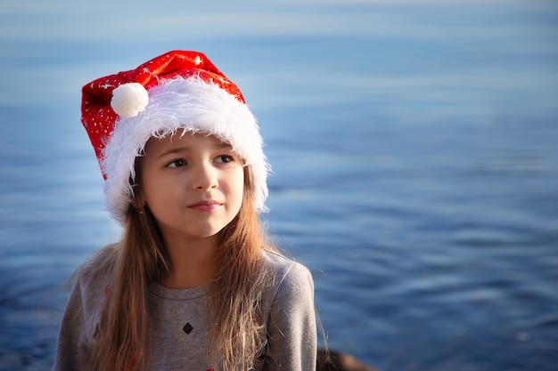 Ein Schulmädchen mit Neujahrshut sitzt am Meer und träumt