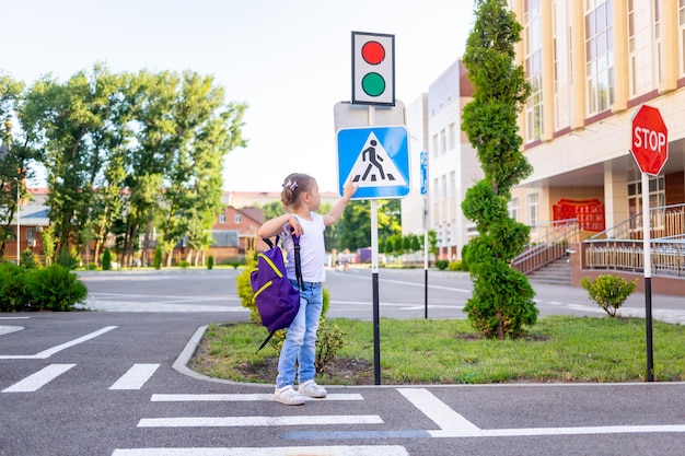 Ein Schulmädchen überquert die Straße auf einem Zebra in der Nähe des Fußgängerüberwegs, der mit einem Rucksack zur Schule geht, das Konzept der Verkehrsregeln