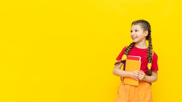 Ein Schulmädchen zeigt auf Ihre Anzeige auf einem gelb isolierten Hintergrund Zusätzliche Schulungen für Schüler Ein glückliches kleines Mädchen zeigt auf die Anzeige