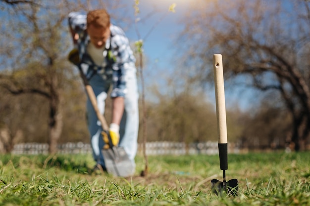 Ein Schuss von einem reifen Kerl, der im Frühling im Garten arbeitet und einen neuen Baum und eine Schaufel Erde gräbt vor