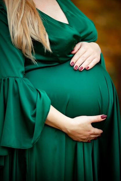 Ein schwangeres Mädchen in einem grünen Kleid umarmt ihr Baby im Bauch und hat eine helle Maniküre