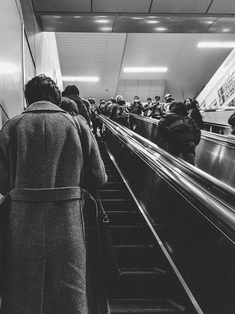 Ein Schwarz-Weiß-Foto einer Frau, die mit einem Mann, der einen Mantel und einen langen Mantel trägt, auf einer Rolltreppe fährt.