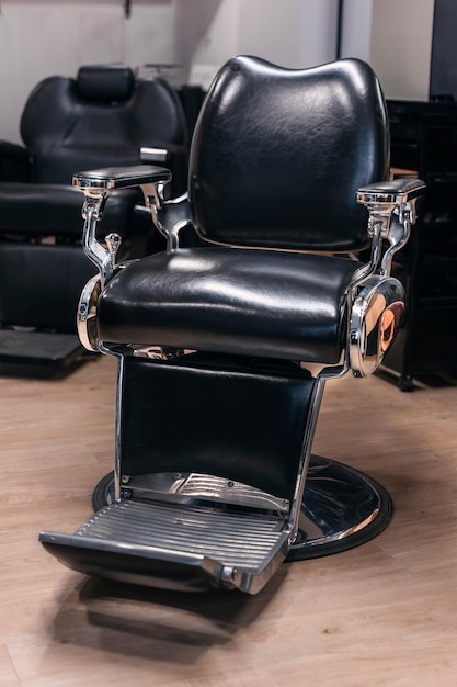 Ein schwarzer Lederbarberstuhl sitzt auf einem Holzboden vertikal