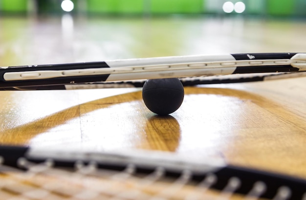 Ein schwarzer Squashball liegt unter einem Tennisschläger auf einem Parkettboden Horizontales Foto