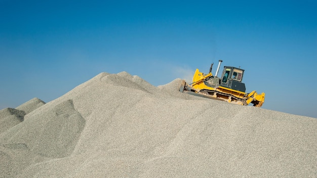 Ein schwerer Bulldozer auf einem Kiesberg, der unter blauem Himmel geladen wird