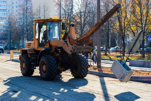 Ein schwerer Frontlader transportiert Erde in einer Schaufel und ebnet die Straße. Straßenreparatur im Zentrum einer modernen Stadt im Herbst. Schwere Baumaschinen zum Bewegen von Erde.