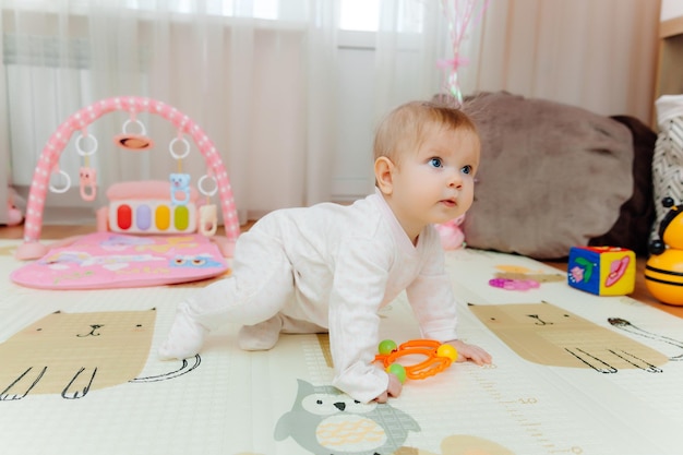 Ein sechs Monate altes Baby spielt mit bunten Spielsachen auf dem Boden Das Baby lernt, Porträt zu kriechen