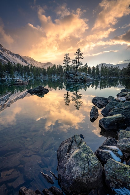 Ein See im Winter, auf dem während eines Sonnenuntergangs ein Felsen mit zwei Bäumen steht