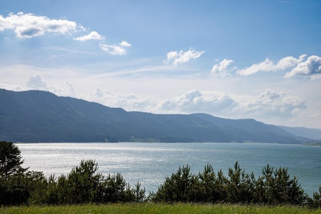 Ein See reflektiert Sonnenlicht gegen blauen Himmel und Bergketten und Dörfer