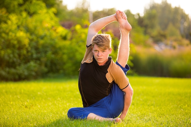 Ein sehr flexibler junger Mann beim Yoga auf dem Rasen bei Sonnenuntergang