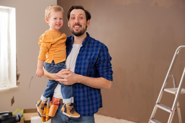 Ein sehr hübscher brünetter Vater hält seinen süßen blonden Sohn in den Armen und sie lachen beide