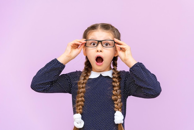 Ein sehr überraschtes und schockiertes Mädchen in einem Kleid und einer Brille auf einem isolierten Hintergrund