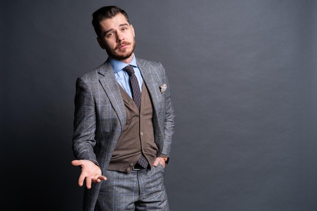 Ein selbstbewusster, eleganter, gutaussehender junger Mann, der vor einem grauen Hintergrund in einem Studio steht und einen schönen Anzug trägt.