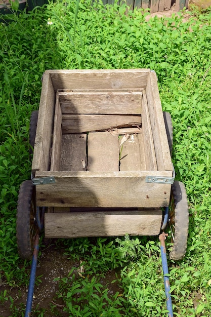 Ein selbstgebauter kleiner leerer Holzwagen mit Griffen steht im grünen Gras