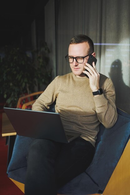 Ein selbstständiger Mann in stilvoller Kleidung erstellt einen Blog-Website-Beitrag auf einem Laptop-Computer in einem modernen Arbeitsbereich Männlicher Freiberufler arbeitet aus der Ferne und telefoniert