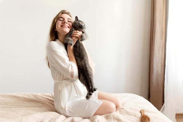 Ein sexy Mädchen in dünnem Pyjama sitzt auf dem Bett und hält ein schönes schottisches Katzen-sexy Mädchen zu Hause im Pyjama auf einem Bett mit einem Haustier