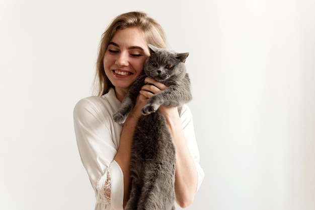 Ein sexy Mädchen in dünnem Pyjama sitzt auf dem Bett und hält ein schönes schottisches Katzen-sexy Mädchen zu Hause im Pyjama auf einem Bett mit einem Haustier