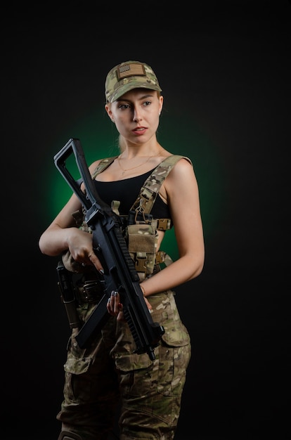 Ein sexy Mädchen in Militär-Airsoft-Overalls posiert mit einem Sturmgewehr auf dunklem Hintergrund