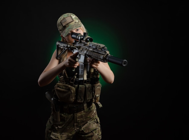 Foto ein sexy mädchen in militär-airsoft-overalls posiert mit einer waffe in den händen auf dunklem hintergrund