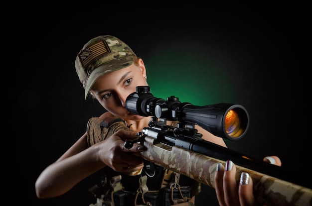 Ein sexy Mädchen in Militär-Airsoft-Overalls posiert mit Scharfschützengewehr auf dunklem Hintergrund