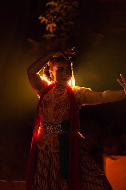 Ein Silhouette-Körper einer balinesischen Frau in einem traditionellen orangefarbenen Kleid, während sie vor der Beleuchtung in der dunklen Nacht tanzt