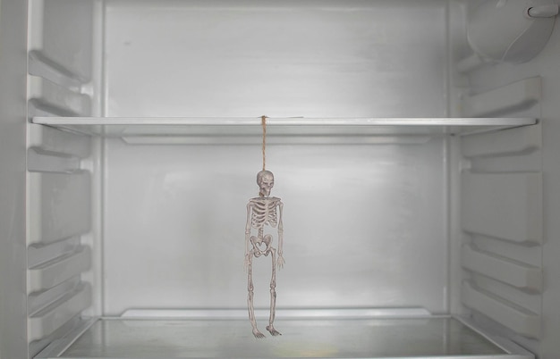 Ein Skelett in einem leeren Kühlschrank Ein Halloween-Witz ist ein Schädel im Kühlschrank in der Küche Absolut kein Essen Das Konzept von nichts zu essen Selektiver Fokus