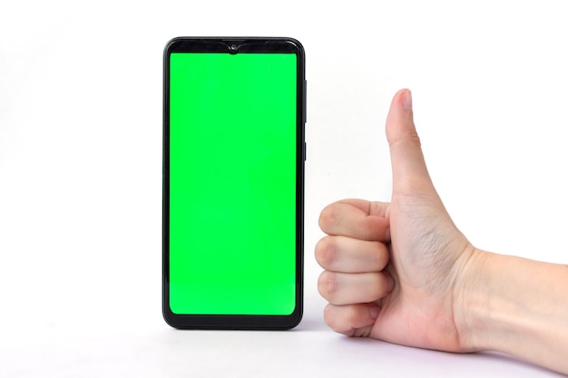 Ein Smartphone in vertikaler Position mit grünem Bildschirm auf weißem Hintergrund und einer Hand mit Daumen nach oben. Chroma-Key. Attrappe, Lehrmodell, Simulation.