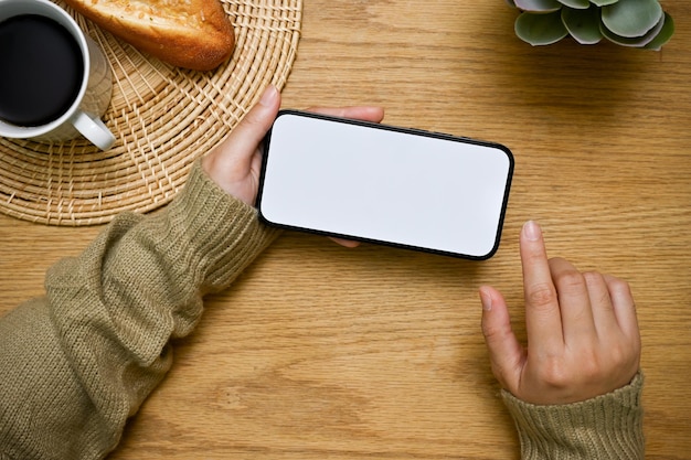 Ein Smartphone-Modell in horizontaler Position befindet sich in der Hand einer Frau über einer hölzernen Tischplatte