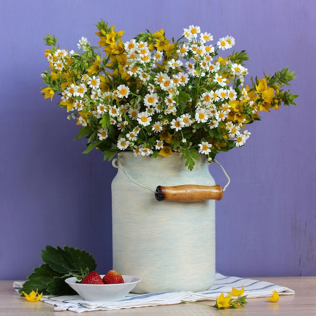 Ein sommerlicher Gartenstrauß in einer Dose und Erdbeeren auf violettem Hintergrund