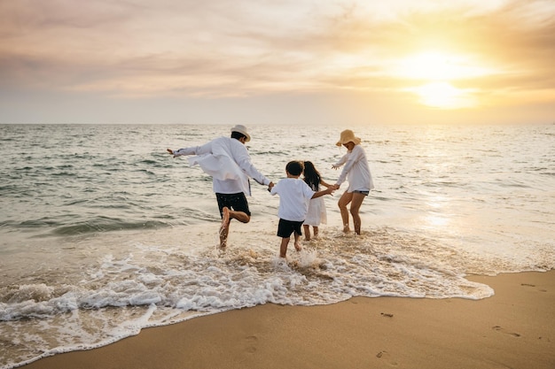Ein sorgloser Tag am Strand für eine asiatische Familie Eltern und Töchter, die von hinten gesehen werden, genießen Bindungsmomente, spielen mit ausgestreckten Armen zu rennen und vorgeben zu fliegen Familienfreude im Sonnenlicht