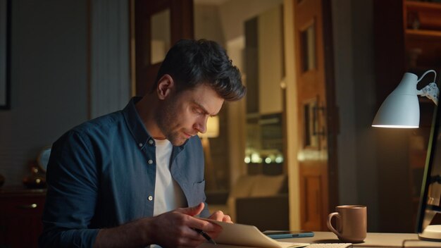 Ein später Schüler blättert ein Notebook um und schaut sich ein Webinar am Abend am Arbeitsplatz an.