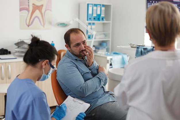 Foto ein spezialisiertes kieferorthopädenteam erklärt patienten mit zahnschmerzen die mundhygiene und diskutiert medizinisches fachwissen während der stomatologischen beratung in der zahnarztpraxis. konzept des medizinischen dienstes