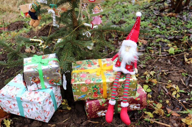 Ein Spielzeug-Gnome sitzt auf Weihnachtsgeschenken unter einem Tannenbaum im Garten horizontale Foto-Closeup
