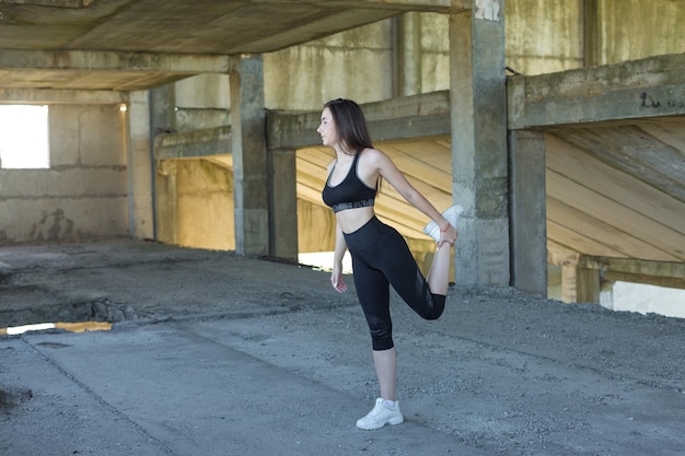 Ein sportlich schlankes Mädchen in Leggings und Top steht an einer Betonwand und führt eine Reihe von Übungen durch