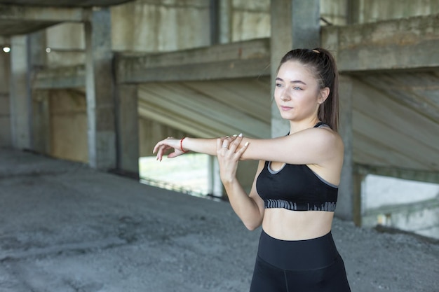 Ein sportlich schlankes Mädchen in Leggings und Top steht an einer Betonwand und führt eine Reihe von Übungen durch