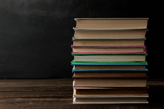 Ein Stapel Bücher auf einem braunen Holztisch und auf schwarzem Hintergrund. Alte Bücher. Ausbildung. Schule. Arbeitszimmer Mit Platz für Inschriften