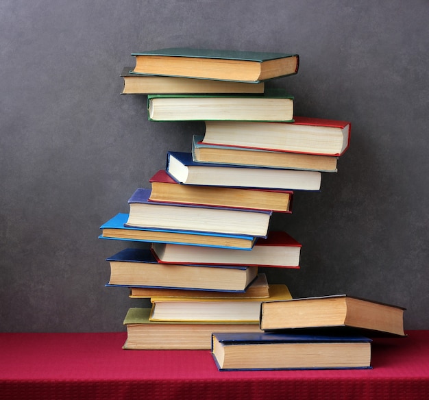 Ein Stapel Bücher in den farbigen Abdeckungen auf dem Tisch mit einer roten Tischdecke. Stillleben mit Büchern.