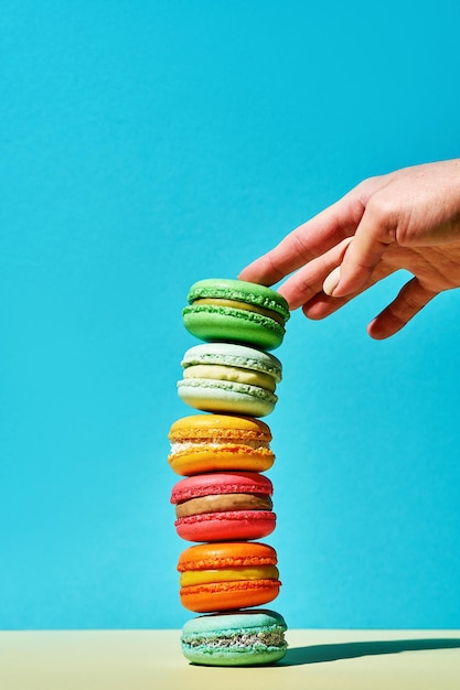 Ein Stapel bunter Macarons, die von der Hand eines Mädchens berührt werden Helle Farben Französisches Gebäck