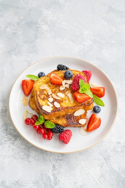 Ein Stapel French Toast auf einem Teller mit frischen Beeren, Mandelblüten und Honig